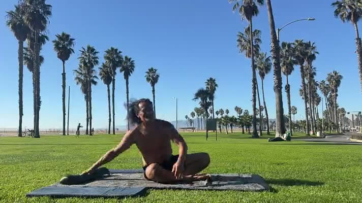 A practitioner seated on a mat in the park