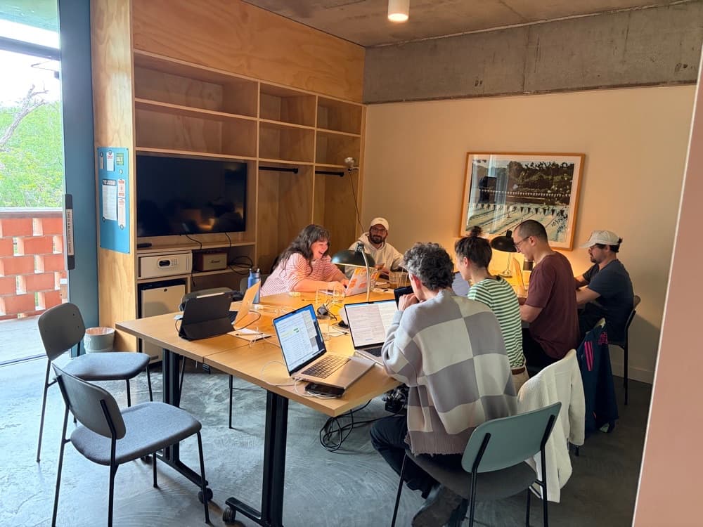 The team gathered around the table in a sunlit plywood workroom